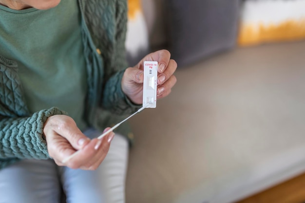 Shot of a woman using cotton swab while doing coronavirus PCR test. Woman takes coronavirus sample from her nose at home. Senior woman at home using a nasal swab for COVID-19.