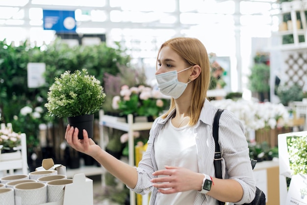 コロナウイルスのパンデミック時に保護マスクを着用し、園芸店で植物を購入している女性のショット。園芸用品店。