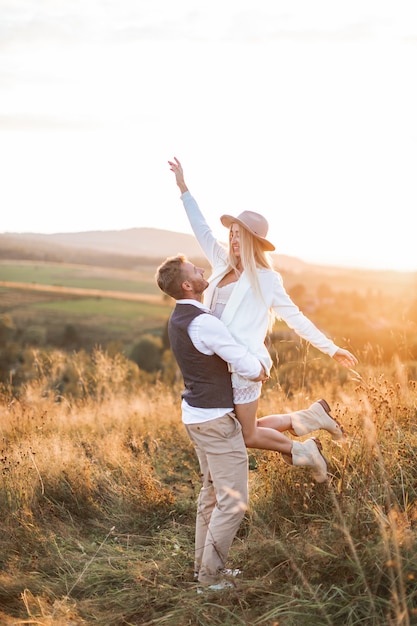 Photo shot of young boho hippie woman being carried by her handsome boyfriend in summer field