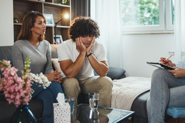 Shot of a young couple during a counseling session with theirs\
female psychotherapist while being seated on a sofa inside of a\
living room.