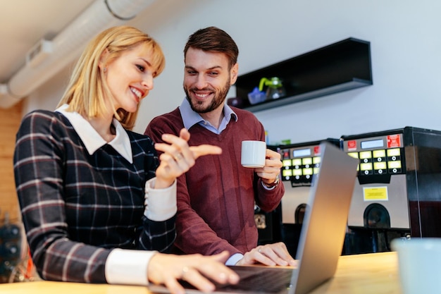 Shot of a young couple talking in an office cafeteria  looking at a laptop computer