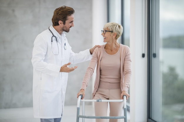 Foto inquadratura di un giovane medico che assiste una paziente anziana a camminare con il suo deambulatore.