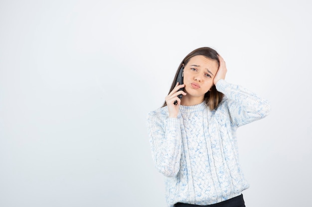 Shot of young girl in sweater talking with someone over cellphone.