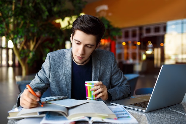 Sparato di giovane studente maschio che si siede alla tavola e che scrive sul taccuino. giovane studente maschio che studia in caffè.