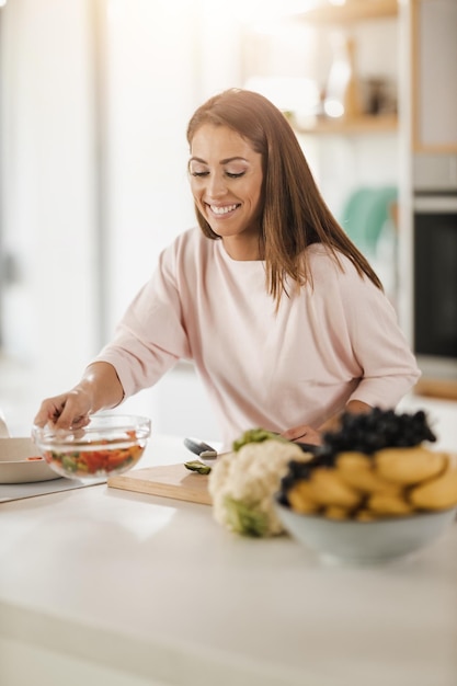 キッチンで健康的な食事を準備している笑顔の若い女性のショット。