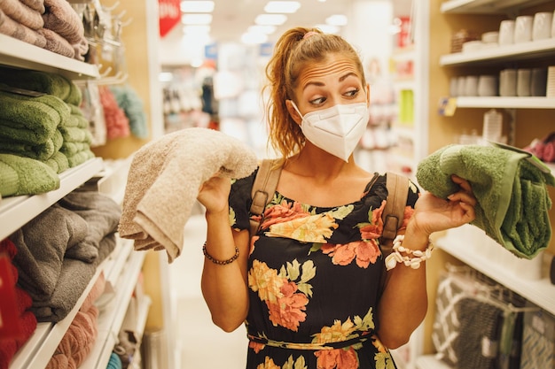 若い女性のショットは、Covid-19パンデミックの間にスーパーマーケットでタオルを購入しているときにN95保護マスクを着用しています。