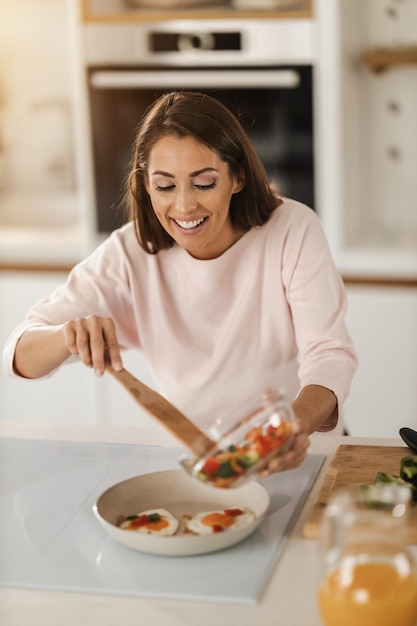 Shot of a young woman preparing a fried egg vith vegetables for breakfast in her kitchen.