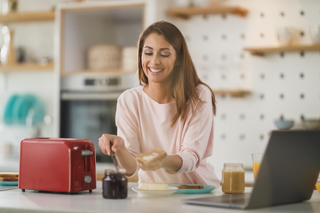 キッチンでトーストにバターを塗る若い女性のショット。