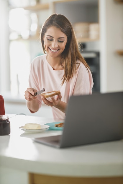 キッチンでトーストにバターを塗る若い女性のショット。