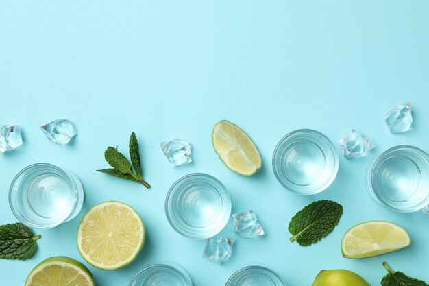 Shots, lime slices, mint and ice cubes on blue wall, top view