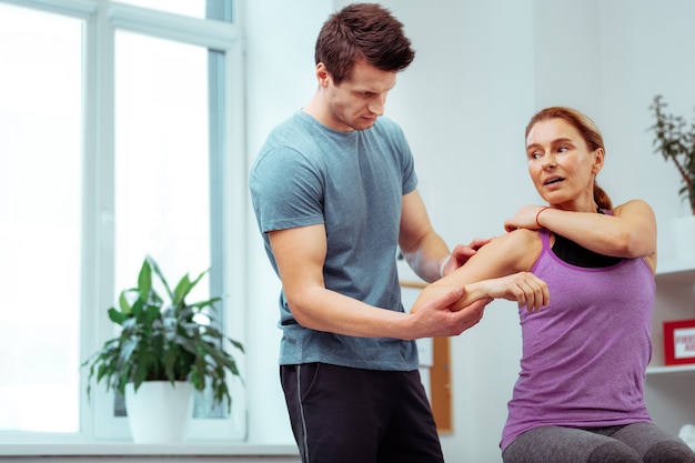 Shoulder massage. Serious male masseur looking at his patients shoulder while doing a shoulder massage