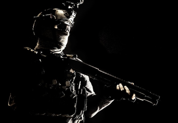 Shoulder portrait of army elite troops soldier antiterrorist tactical team wit shotgun helmet with thermal imager hiding face behind mask armed rifle with optical scope studio shoot on black