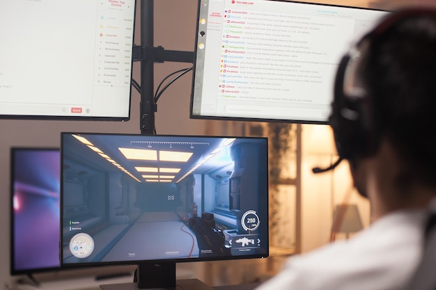 Photo over shoulder shot of man playing shooter game on computer. multiple monitors.