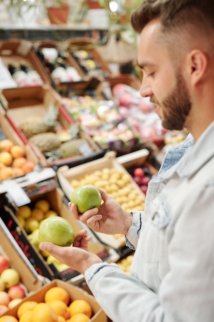 食品売り場に立って、市場での免疫力を強化するために柑橘系の果物を購入しているひげを生やした男の肩越しに見る