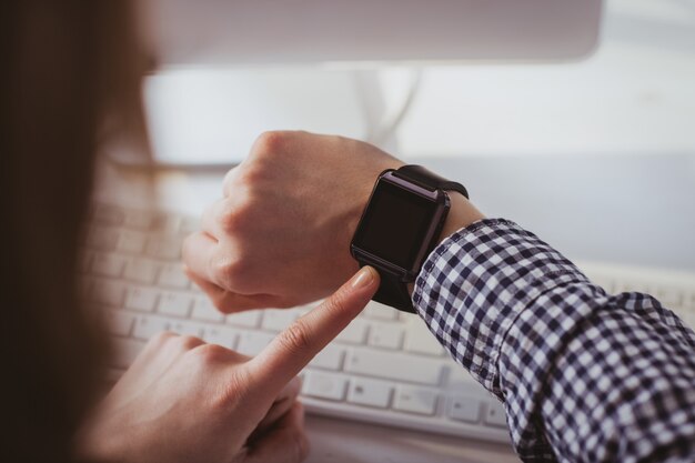 Foto sopra la vista della spalla della donna di affari che usando il suo orologio astuto al suo scrittorio in ufficio