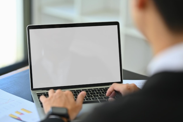 Over shoulder view of male financier using laptop at office desk