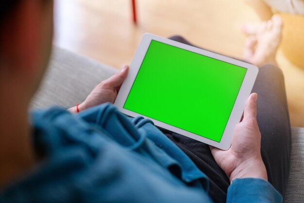 Over the shoulder view of a man working on a tablet with a green chroma key screen while sitting on