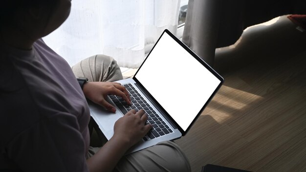 노트북 컴퓨터를 사용하고 거실 바닥에 앉아 있는 뚱뚱한 여성의 어깨 너머로