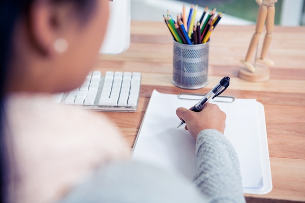 Over shoulder view of woman writing on white sheet in office