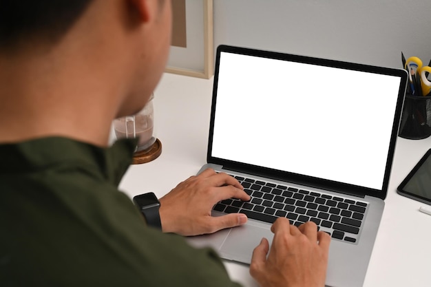 Вид через плечо молодого человека, использующего ноутбук на белом столе