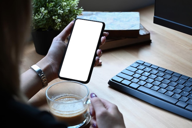 Over shoulder view of young woman drinking coffee and using smart phone at home