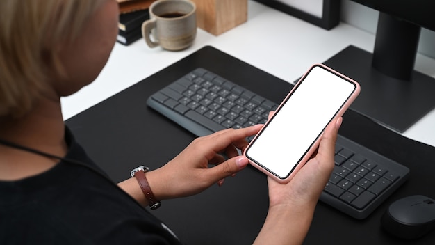 Over shoulder view of young woman hands holding smart phone with blank screen.