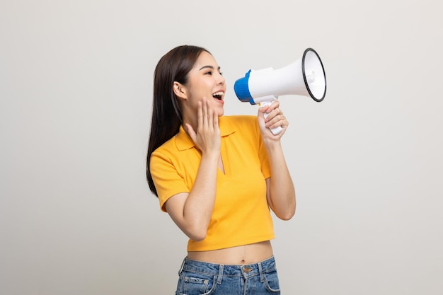 Shout out loud with megaphone. Young beautiful asian woman woman announces with a voice about promotions and advertisements for products at a discounted price. Shopping and fashion concept.