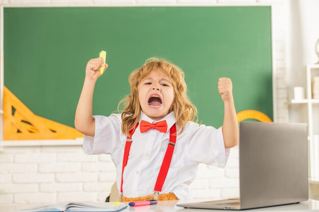 Shouting kid boy in bow tie study in school classrrom at blackboard emotions