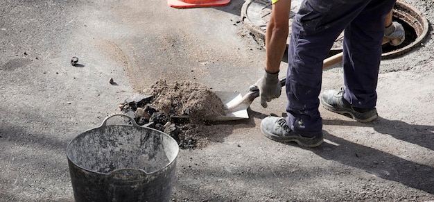 Shovel with stone rubble in the hands of an operator in uniform\
cutting the asphalt ground, dust in