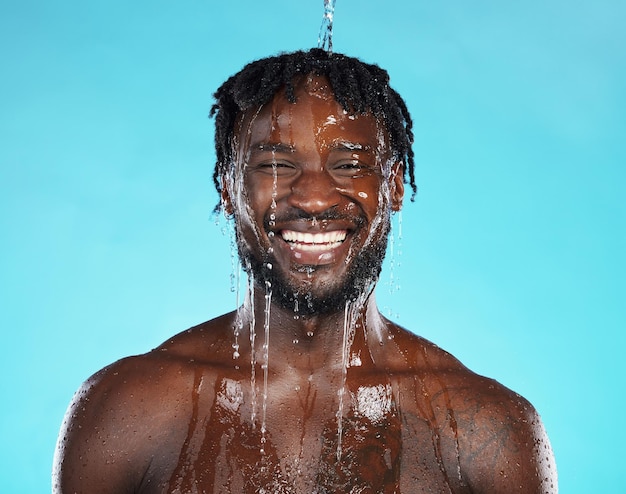 shower portrait and black man isolated on blue background with water drops for face cleaning body and skincare glow strong beauty and happy model or person in studio headshot washing for hygiene