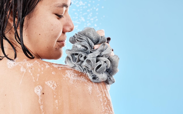 シャワースポンジと水石鹸の泡で体を掃除する女性とモックアップスタジオの青い背景にウェルネス個人衛生と化粧品のためのスキンケアアジアの女の子モデルの美しさとヘチマ付きのお風呂