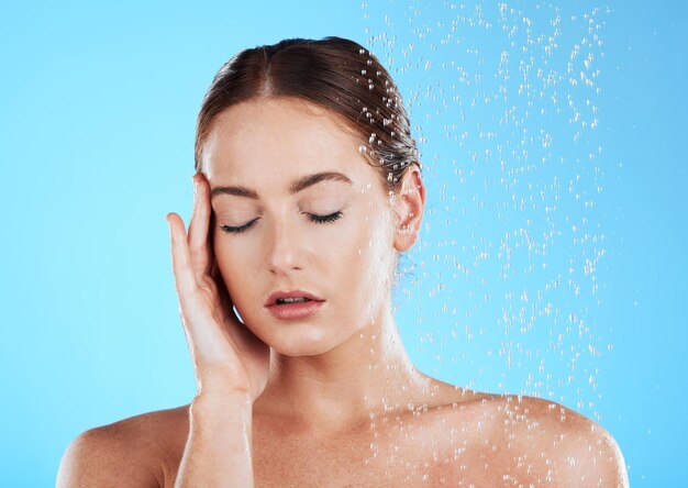 Foto doccia acqua e relax donna in studio sentendosi felice dalla pulizia e dalla cura della pelle spruzzi di benessere e routine di bellezza di una modella femminile eccitata dalla dermatologia e dalla cura di sé con sfondo blu