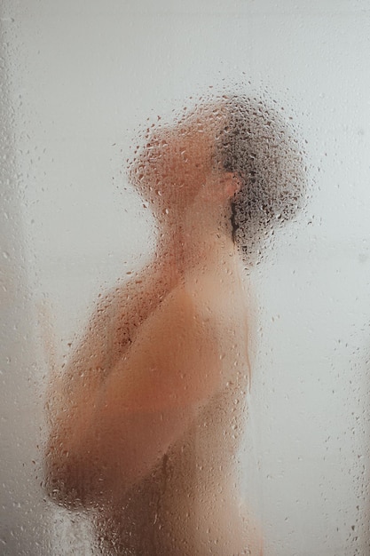 Showering woman behind glass door with water drops