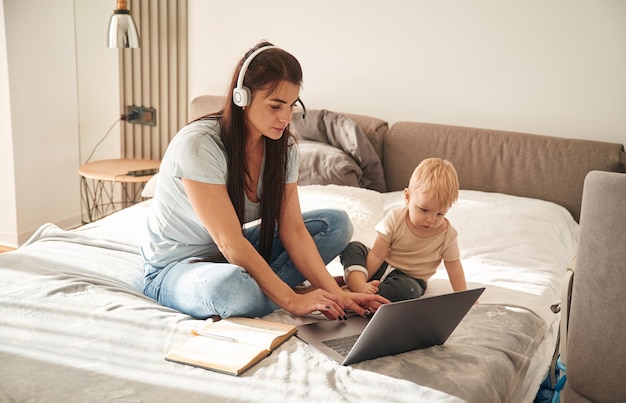 Photo showing laptop mother with her little son is at home in domestic room