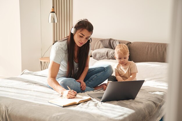 ラップトップを示す母親と彼女の小さな息子は家庭の部屋で家にいる