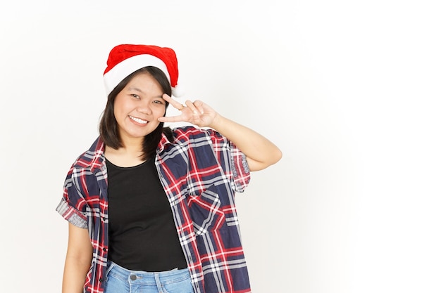 빨간 격자 무늬 셔츠와 산타 모자를 쓰고 아름 다운 아시아 여자의 평화 또는 승리 표시를 보여주는