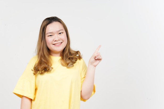 Показ продукта и указание стороны красивой азиатской женщины в желтой футболке, изолированной на белом