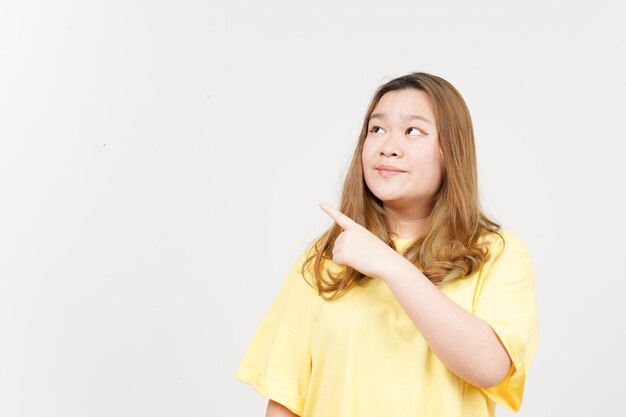 흰색에 고립 된 노란색 티셔츠를 입고 아름 다운 아시아 여자의 제품 및 가리키는 측면을 보여주는