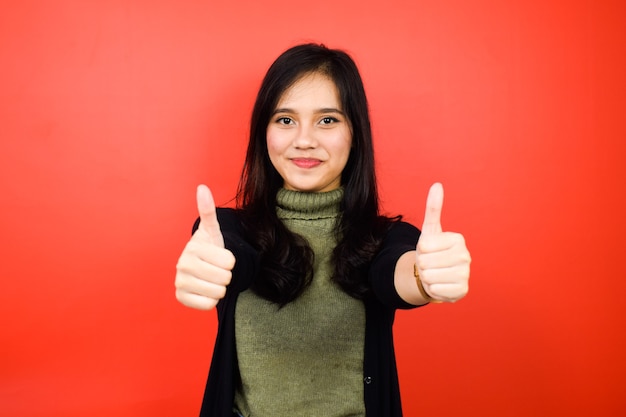 Showing thumbs up Approve sign of Young beautiful asian women using black sweater isolated on red