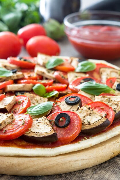 Showing vegetarian pizza with eggplant, tomato, black olives, oregano and basil on wooden table