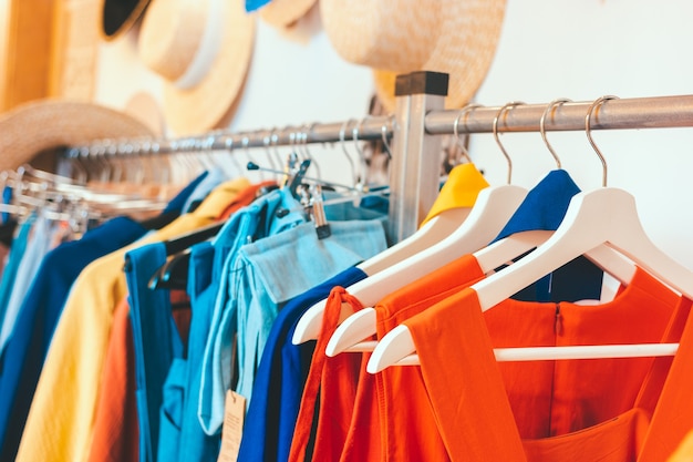 Showroom store of women's clothing and summer straw hats hang on the wall. Rack hanger with colorful outfits. Modern minimalistic interior