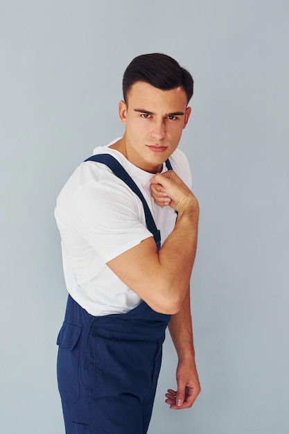 Shows biceps Ready to work Male worker in blue uniform standing inside of studio against white background