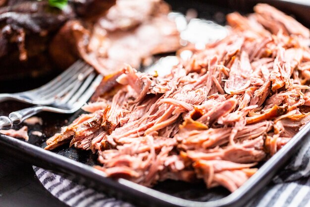 Shredded cooked pork with forks on a baking sheet.