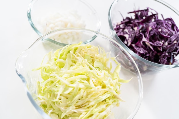 Shredded green and red cabbage in a glass mixing bowl.