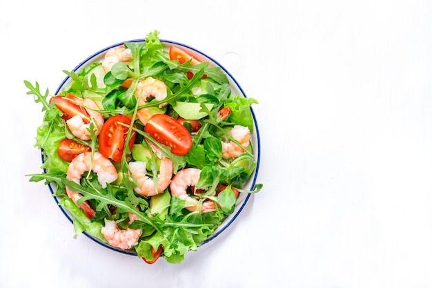 Shrimp salad with cherry tomatoes arugula avocado and oil lemon dressing on white background Top view