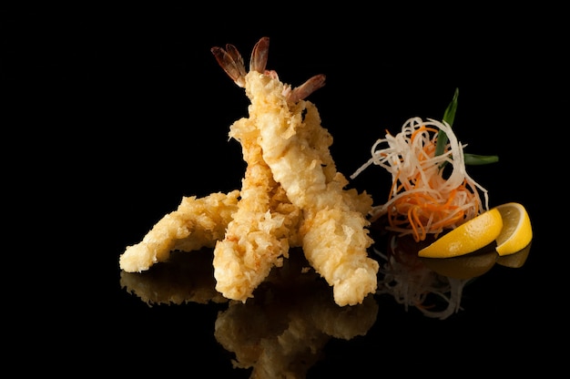 Photo shrimp in tempura with lemon slices and salad on a black background with reflection