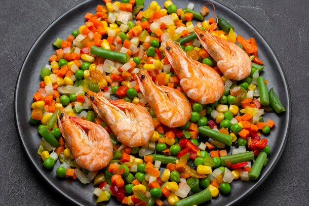 Shrimp with mixed vegetables and green asparagus on black plate Top view Black background