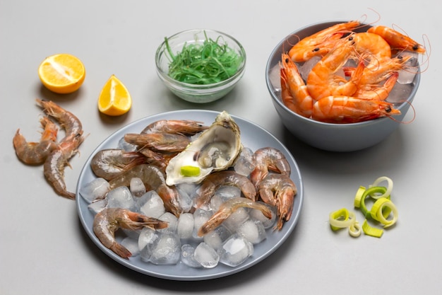 Shrimps on ice on two gray plates Onion seaweed and lemon on table Top view Gray background