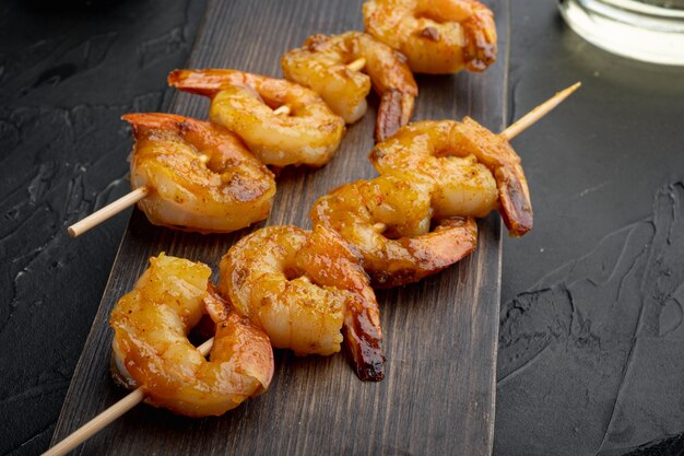 Shrimps on skewers with Mango chutney curry sauce set, on wooden serving board, on black