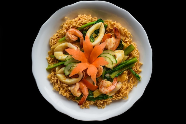 Shrimps and squid with noodles and vegetables in a white bowl isolated on black background top view